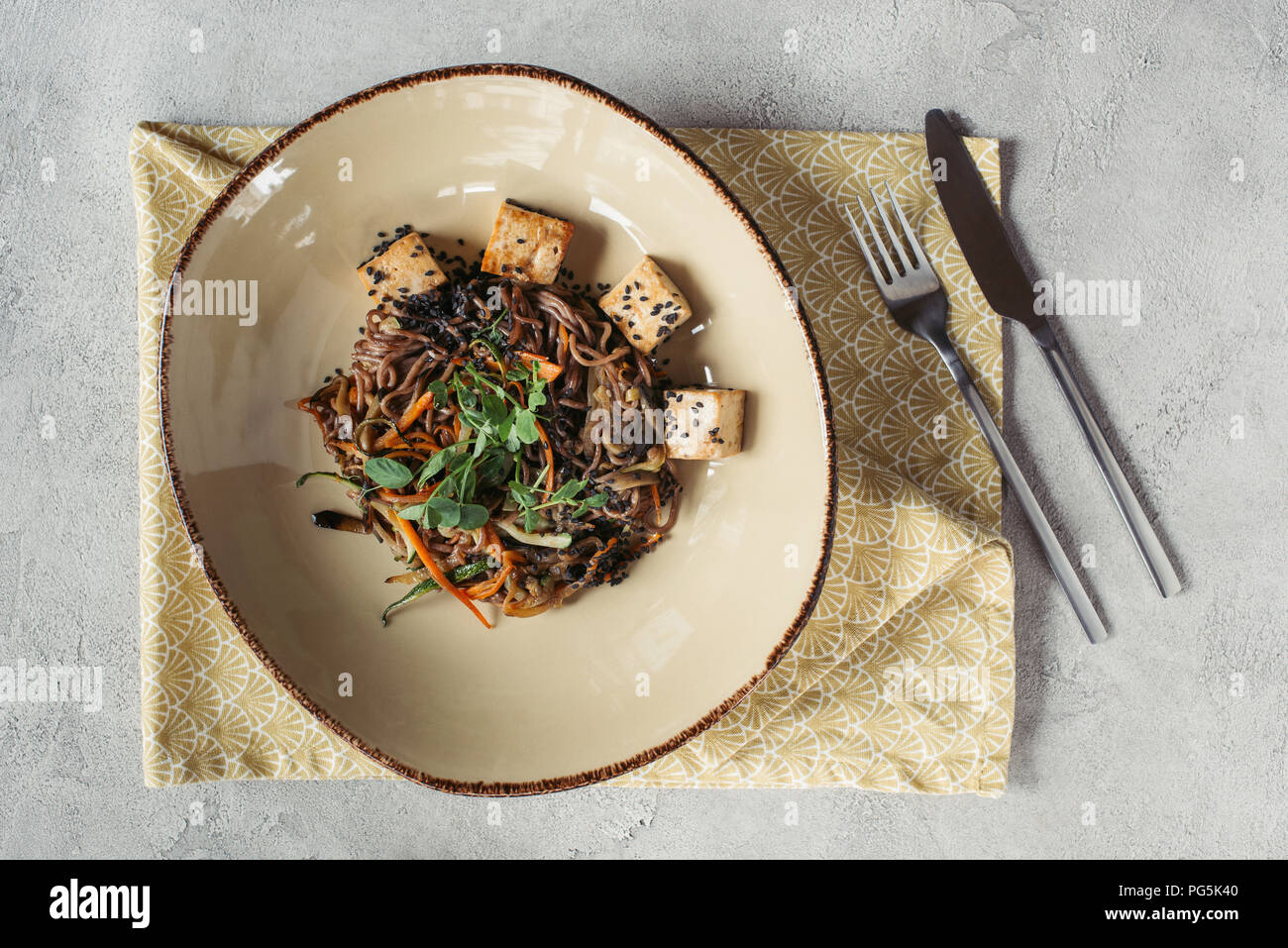 Composizione alimentare con soba con tofu e verdure decorate con semi germinati di girasole sul piano portapaziente grigio Foto Stock