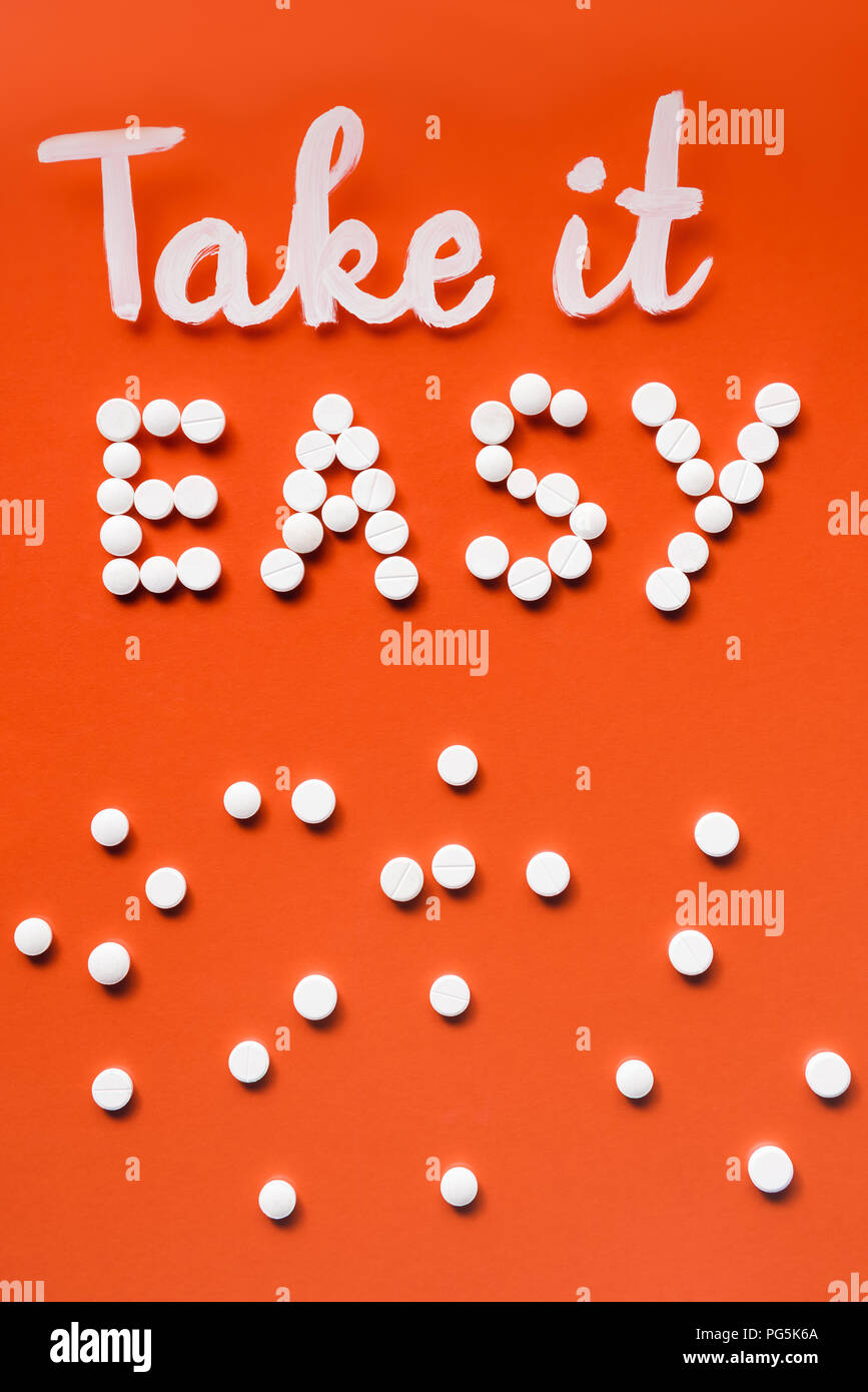 Vista superiore del lettering take it easy da pillole di bianco su sfondo rosso Foto Stock