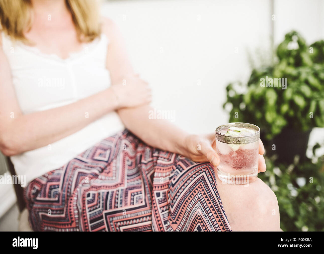 Donna bionda rilassante sul patio holding bevanda ghiacciata Foto Stock