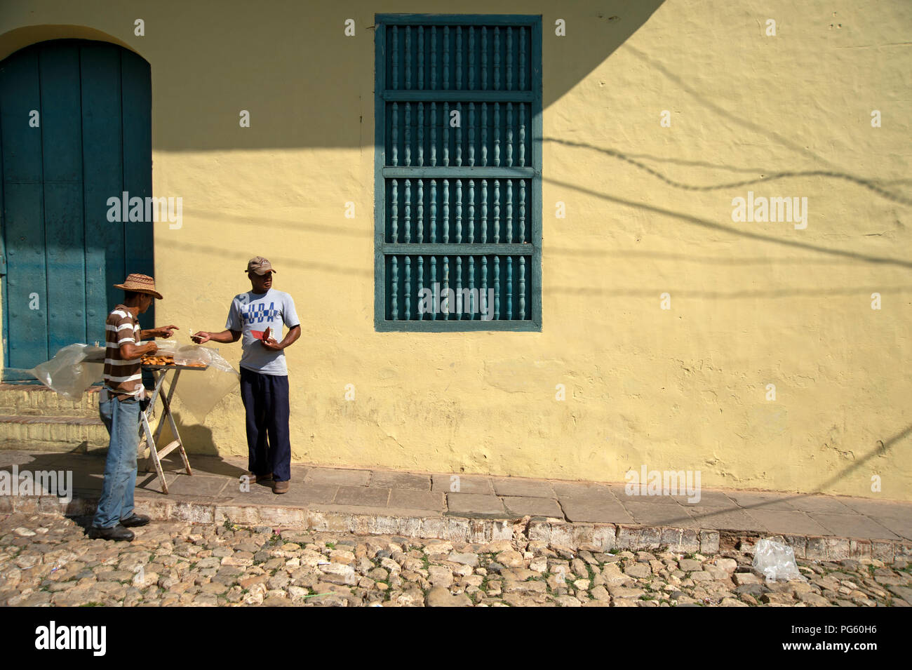 Un uomo cubano comprare una strada snack da un fornitore nelle stradine di Trinidad, Cuba Foto Stock