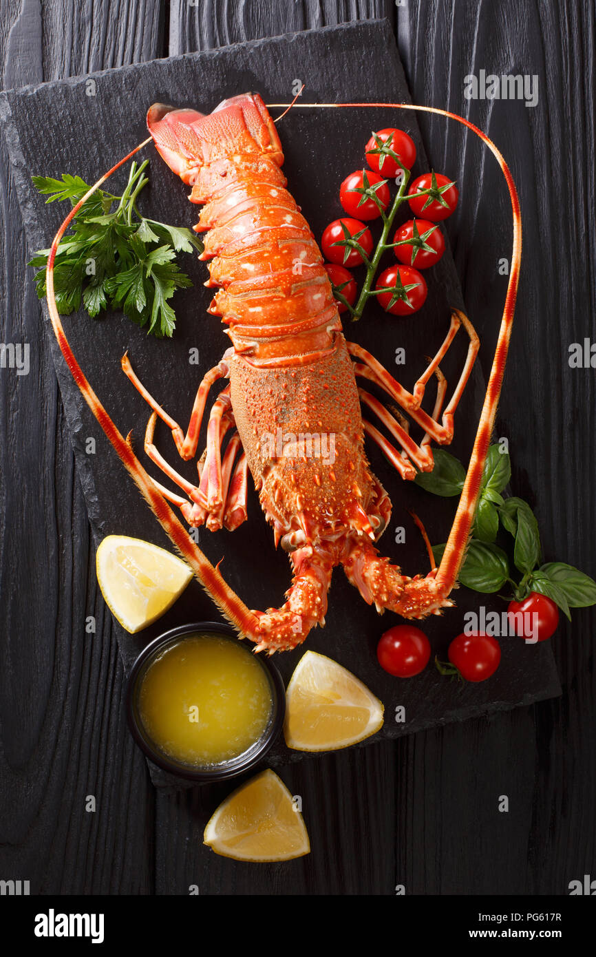 Cibi costosi: spinoso aragosta bollita con pomodoro fresco, succo di limone e il burro fuso close-up sulla pietra nera. Verticale in alto vista da sopra Foto Stock