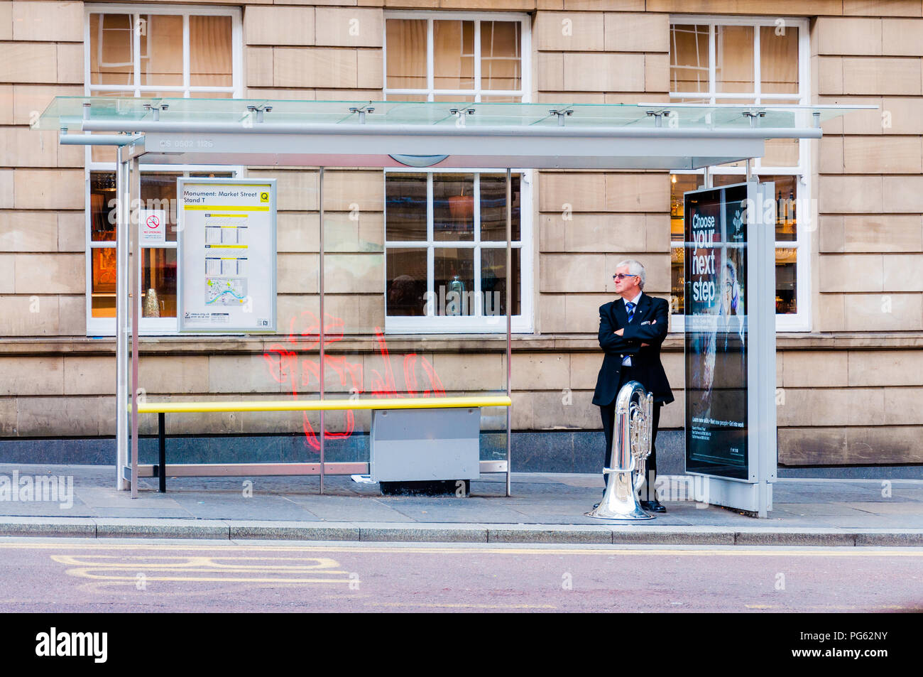Un musicista con la sua tuba in attesa ad una fermata di autobus di Newcastle, England, Regno Unito Foto Stock