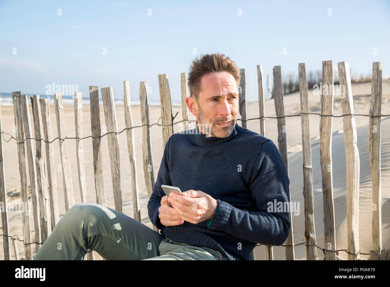 L'uomo con un telefono cellulare seduti al recinto sulla spiaggia Foto Stock
