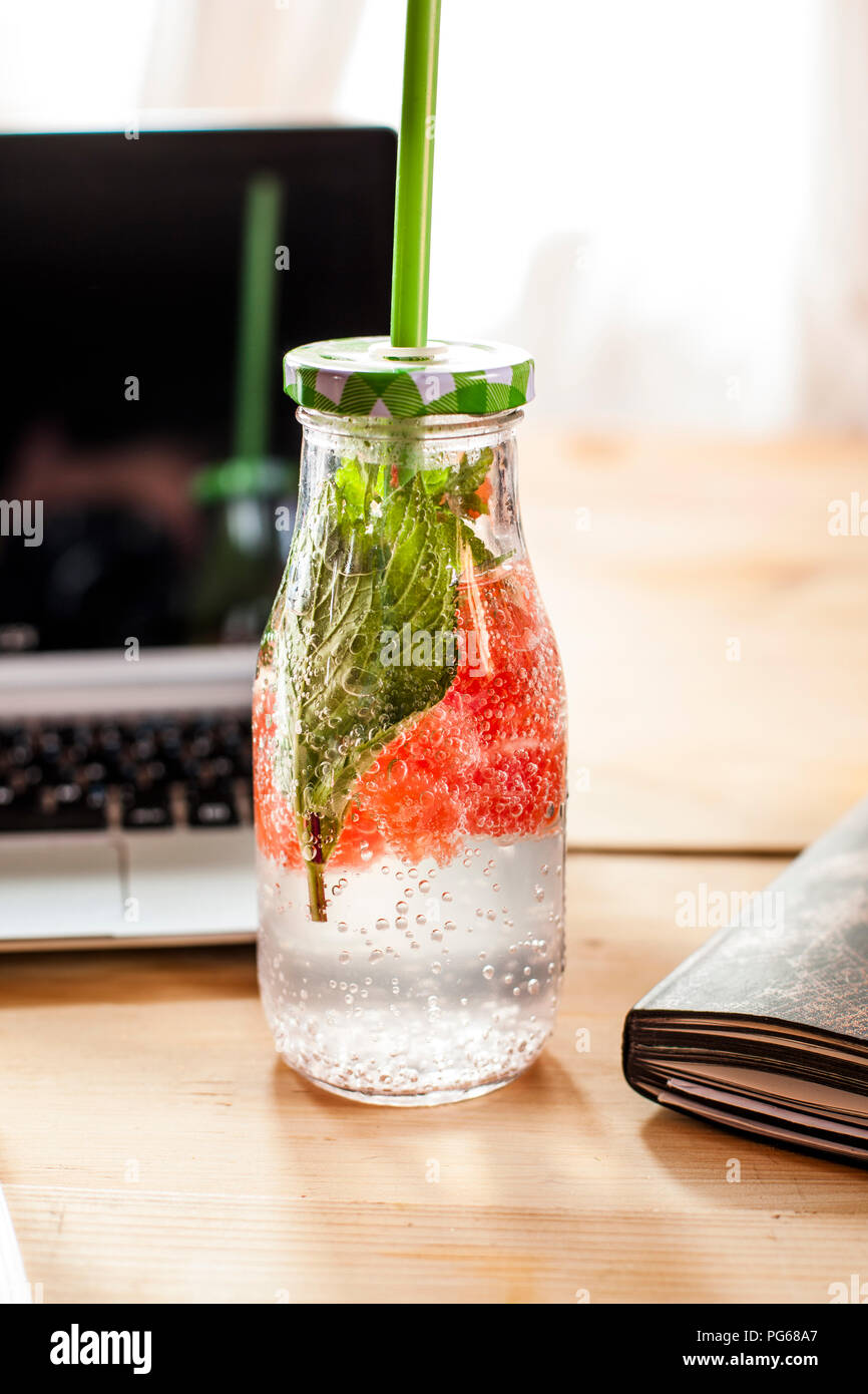Bottiglia di vetro di acqua detox infusi con pompelmo rosso e menta sulla scrivania Foto Stock