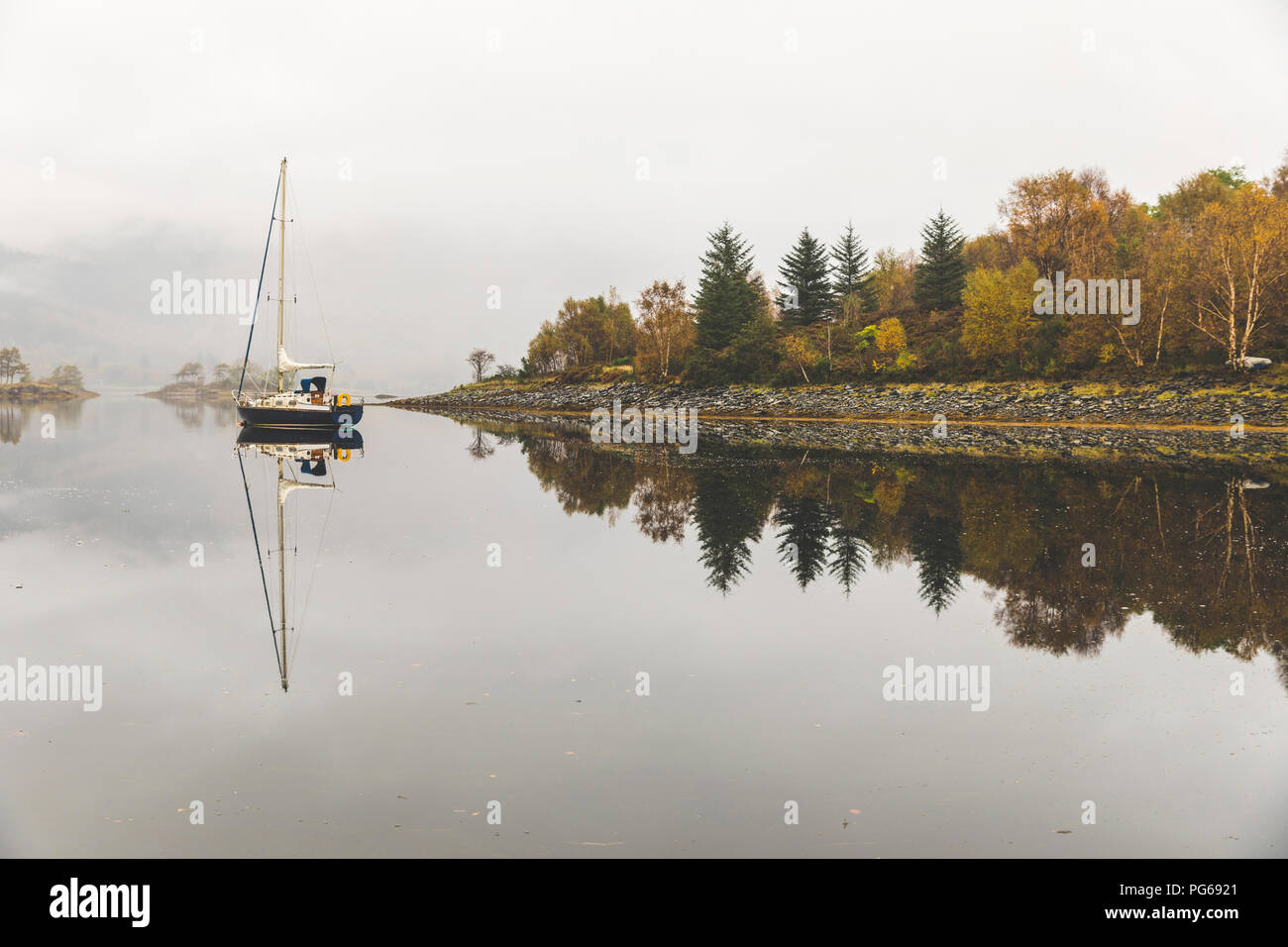 Regno Unito, Scozia, barche a vela e albero riflessioni su un lago nelle highlands Foto Stock