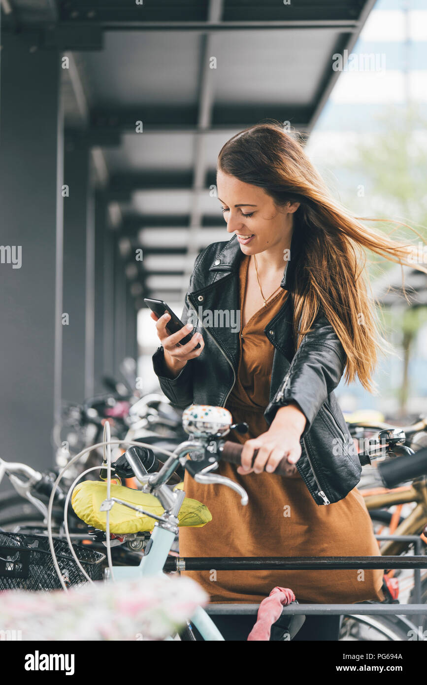 Sorridente giovane donna con la bicicletta utilizzando il cellulare in città Foto Stock