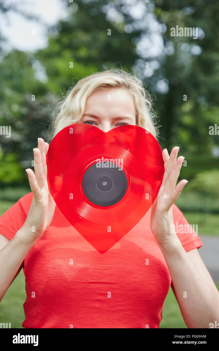 Donna che mantiene un cuore a forma di record di vinile all'aperto Foto Stock