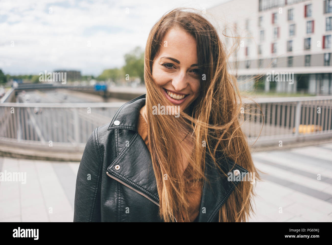 Ritratto di sorridente giovane donna con capelli spazzate dal vento sul ponte autostradale Foto Stock
