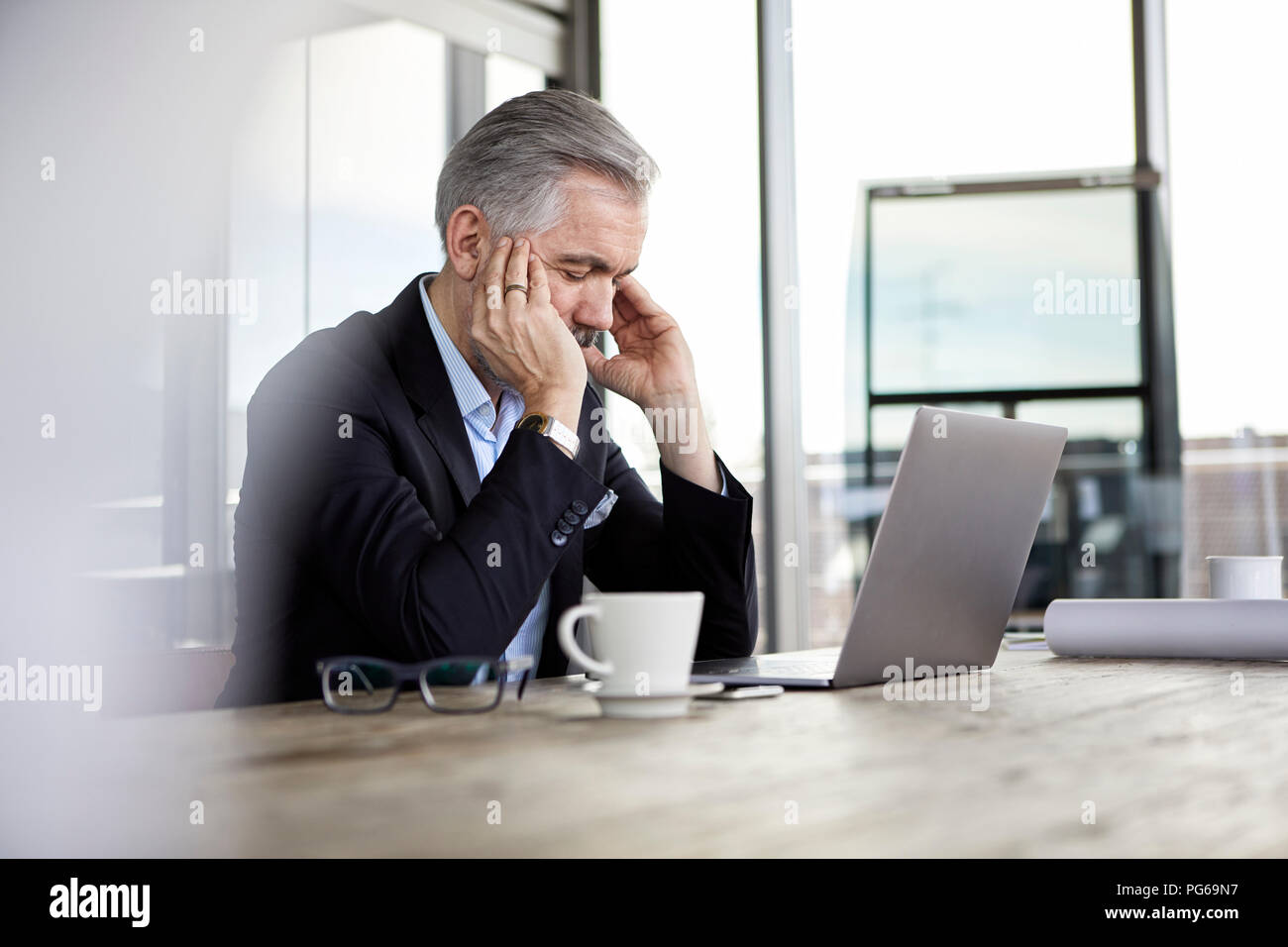 Imprenditore con mal di testa seduto alla scrivania in ufficio Foto Stock