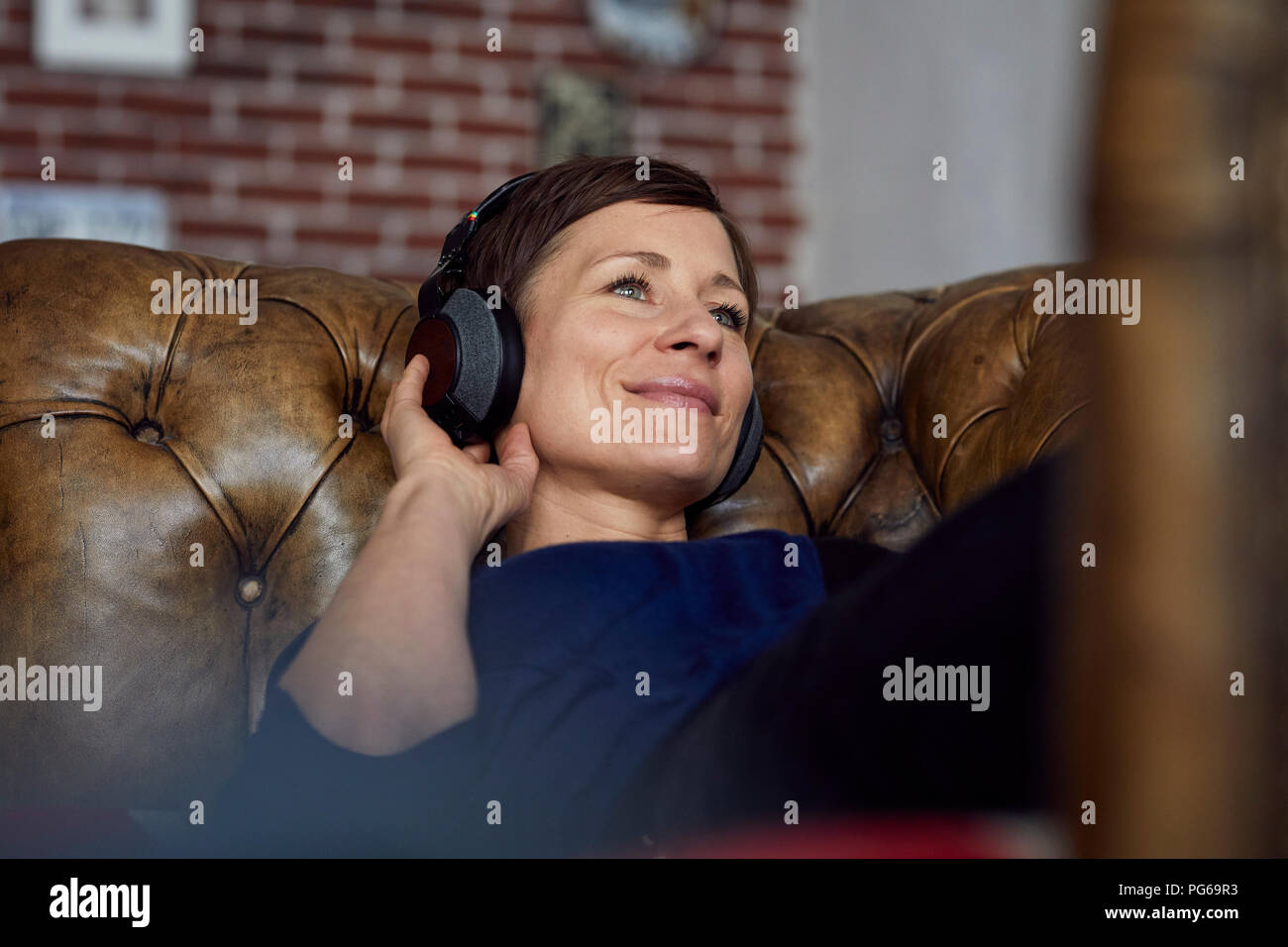 Donna con cuffie sdraiato sul divano e ascoltare della musica Foto Stock