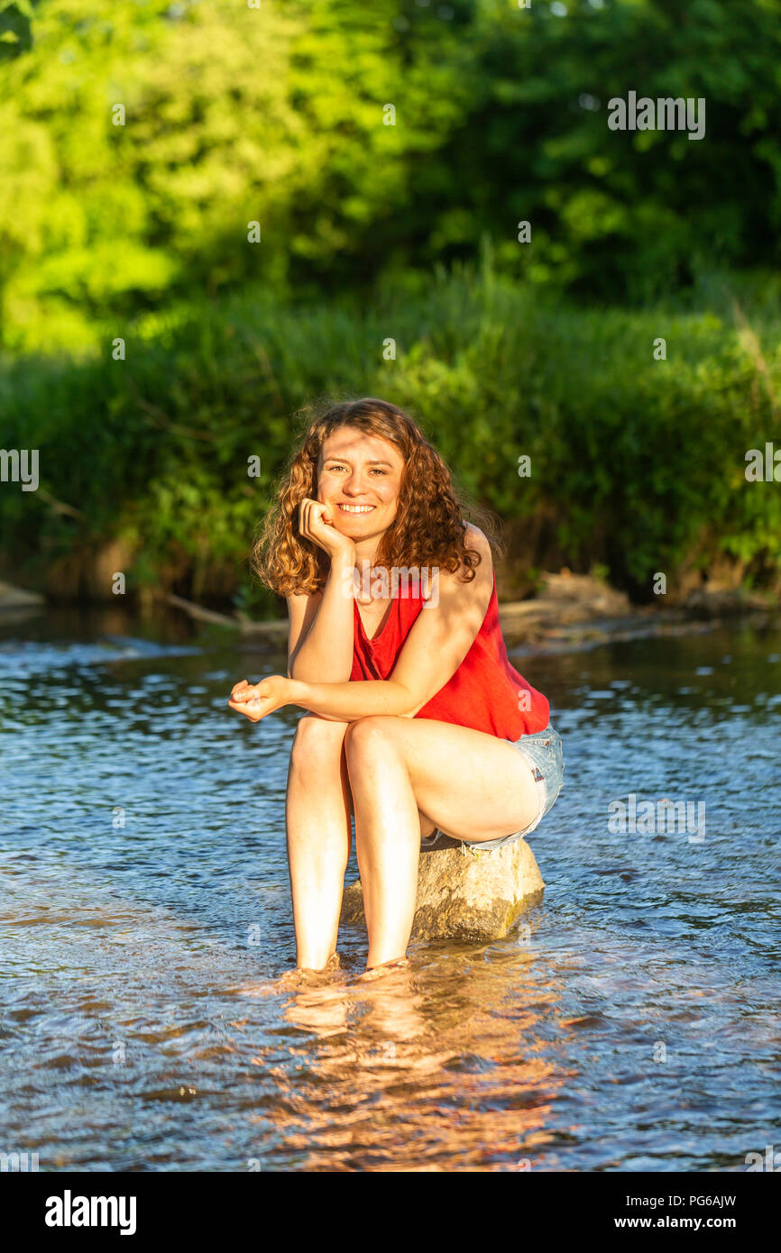 Giovane donna seduta su pietra, Fiume Foto Stock