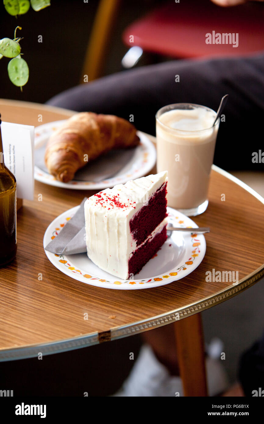 Torta di fantasia, croissant e un bicchiere di latte macchiato su un tavolo Foto Stock
