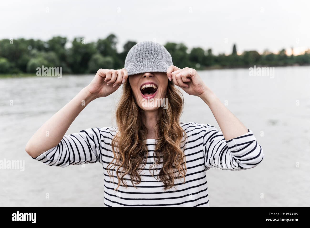 Ridendo donna giocando con wooly hat in corrispondenza di un fiume Foto Stock