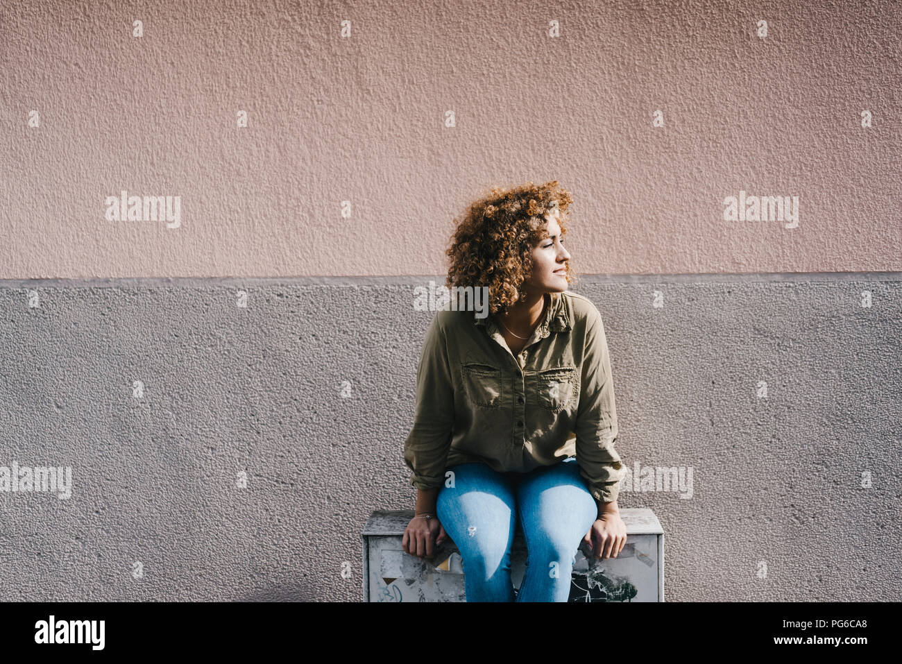 Donna seduta davanti al muro di casa, godendo il sole Foto Stock