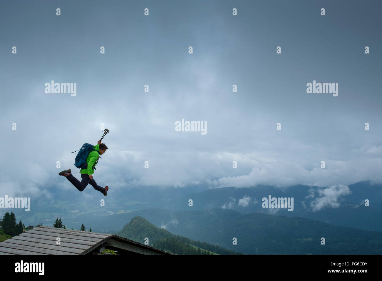 Germania, Brauneck, giovane escursionista con bastoni da trekking e zaino saltare in aria Foto Stock