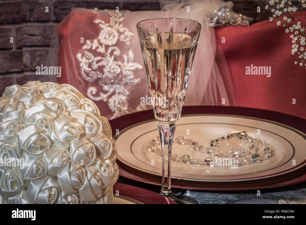 Sposa di guida al tavolo nuziale con bouquet, velo, collana e champagne Foto Stock