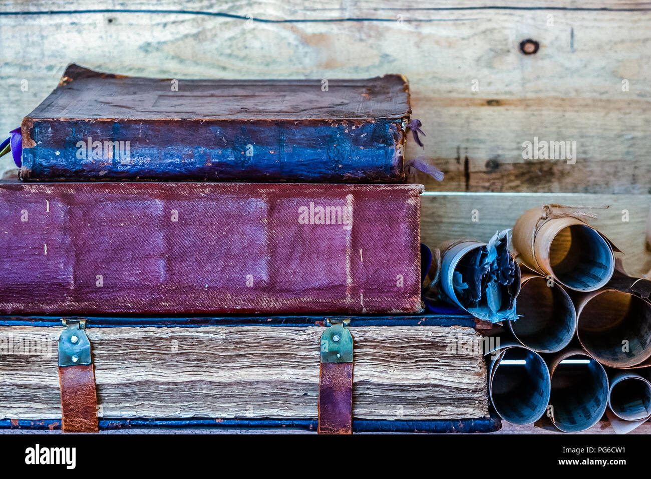 Pila di tre antichi libri su uno scaffale di legno dalla parete in legno. Un mucchio di antiche scorre a destra di libri. Un mazzetto di quills in uno dei rol Foto Stock