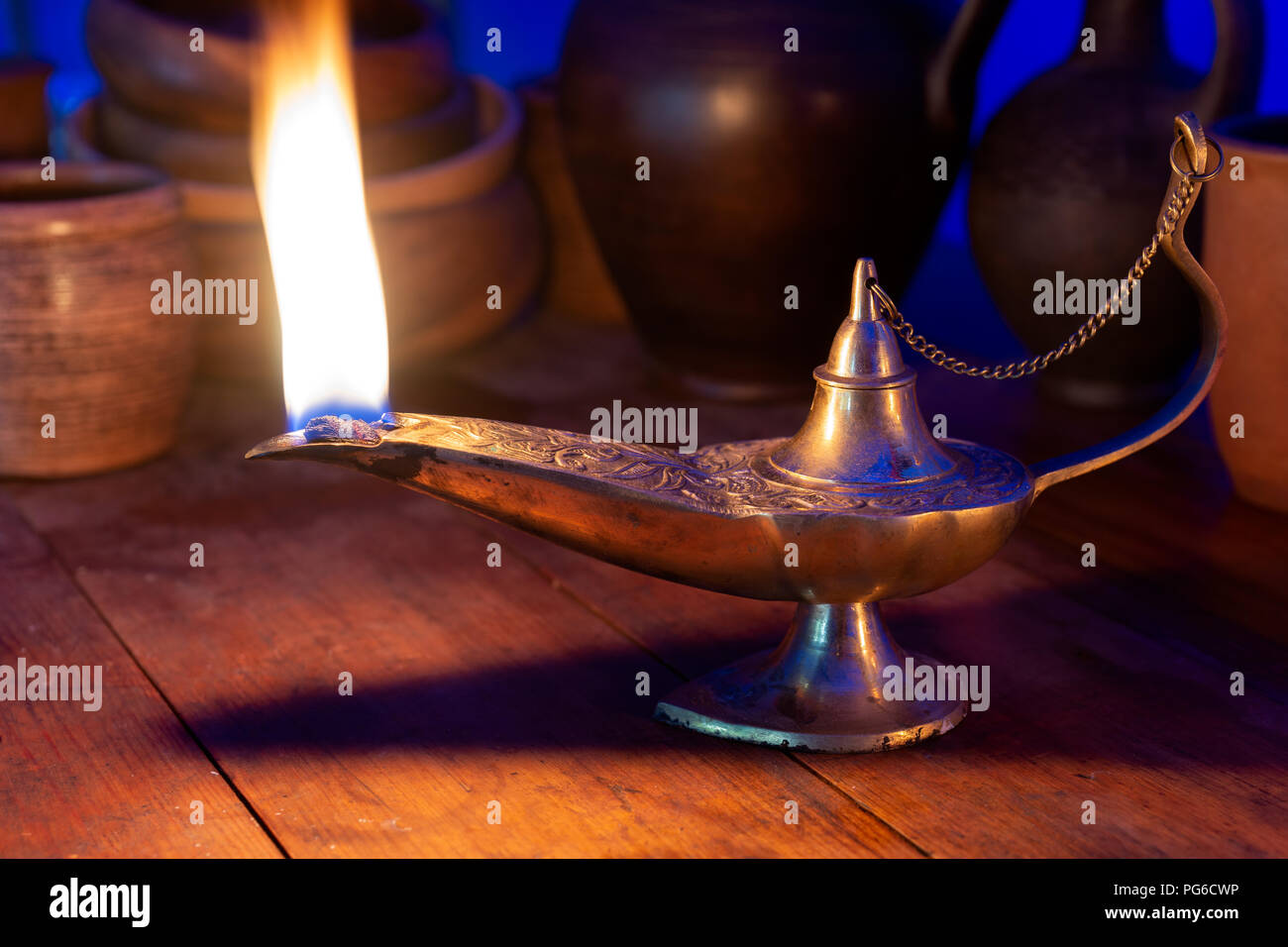 Bella antica olio lampada in bronzo arde su un tavolo di legno. Ceramica in background. Concetto di meraviglioso Aladdin's Lamp pieno di forze magiche Foto Stock
