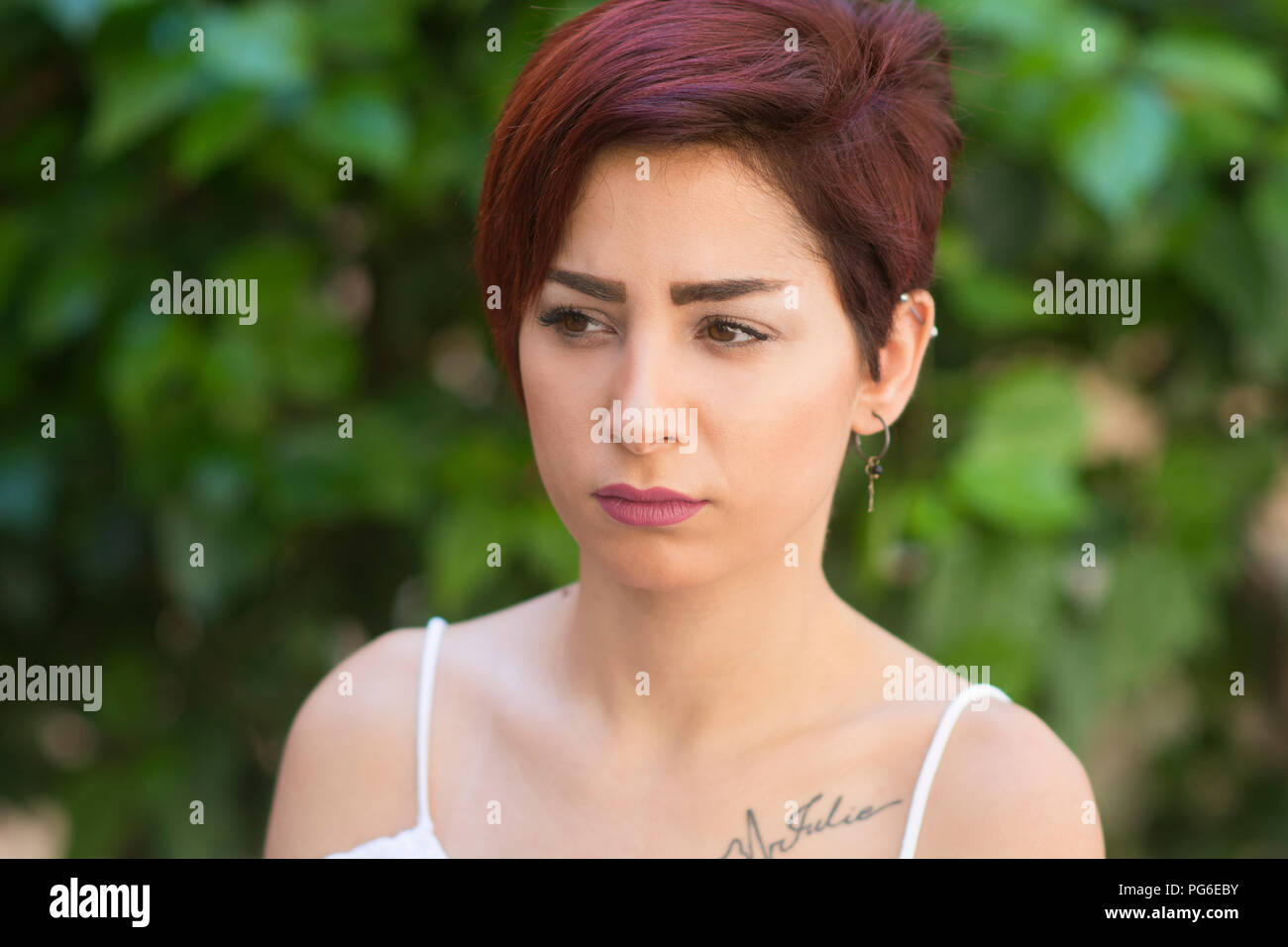 Pensieroso giovane donna con capelli corti che guarda lontano all'aperto Foto Stock