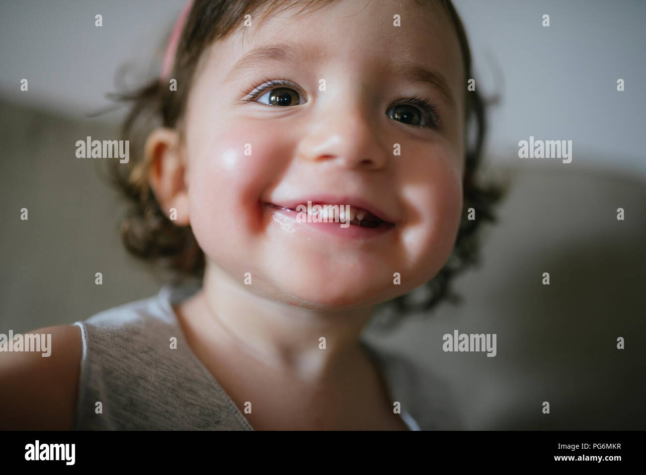 Happy baby ragazza con un grande sorriso comodamente seduti sul divano di casa Foto Stock Happy baby ragazza con un grande sorriso comodamente seduti sul divano di casa Foto Stock