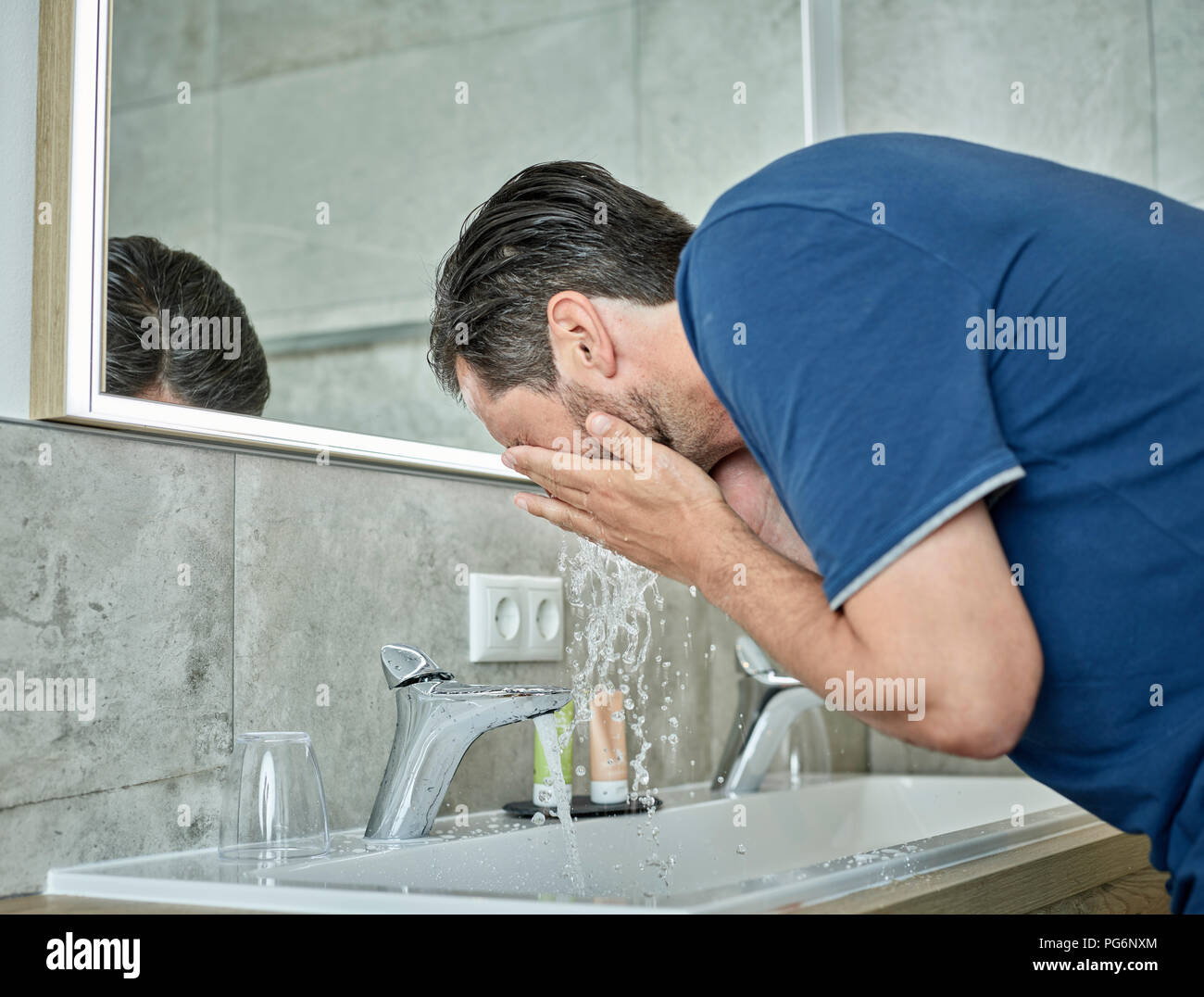 Lavaggio uomo il suo volto nella stanza da bagno Foto Stock