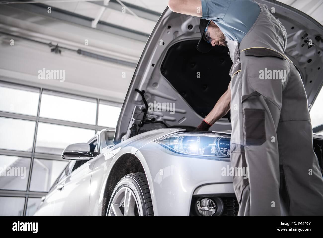 Certificata moderno servizio auto. Caucasian meccanico nel suo 30s controllo elementi cruciali del motore durante il programmato di manutenzione in garanzia. Foto Stock