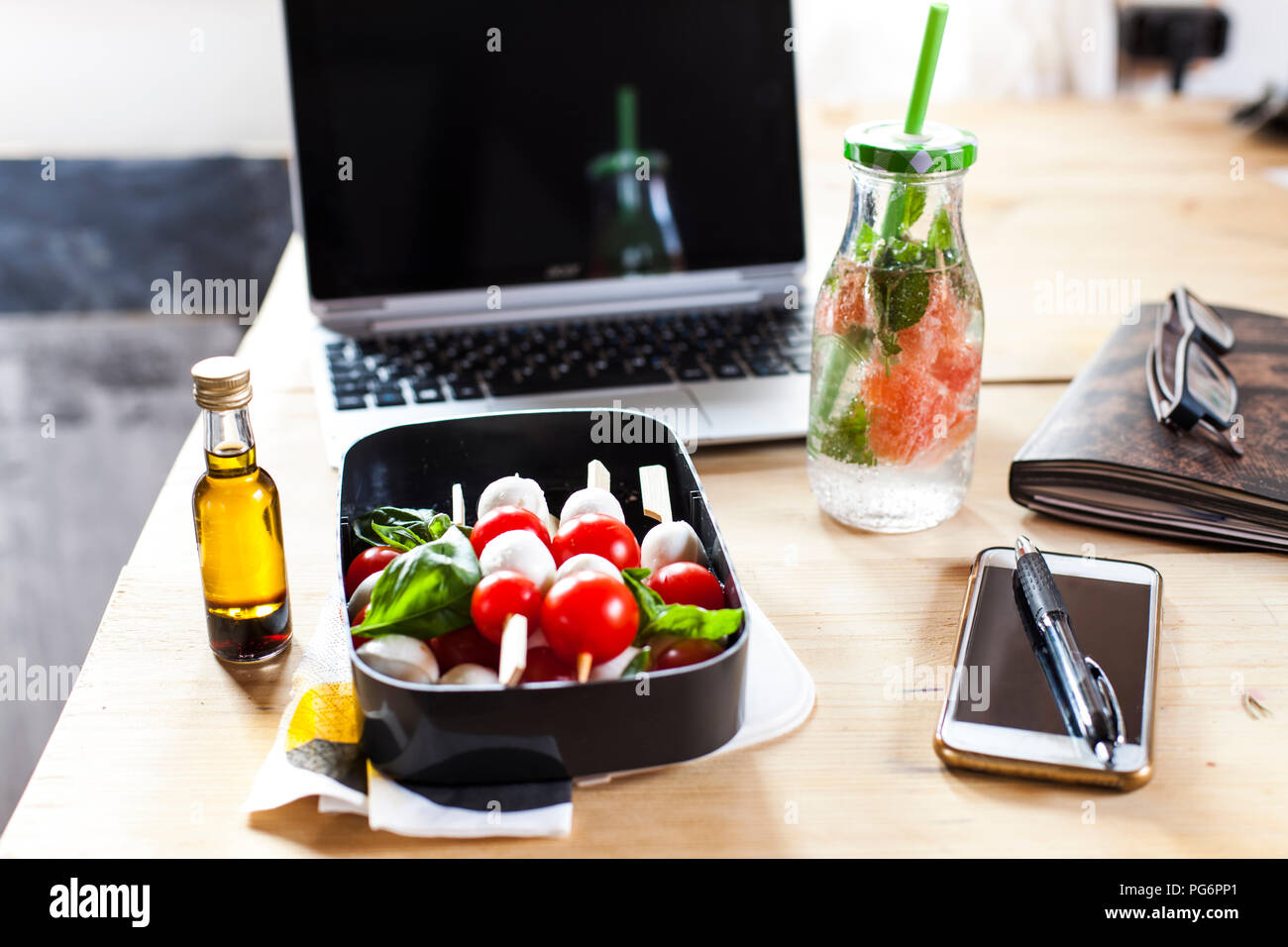 Scatola di pranzo di insalata caprese, bottiglia di acqua infusa e laptop sulla scrivania Foto Stock