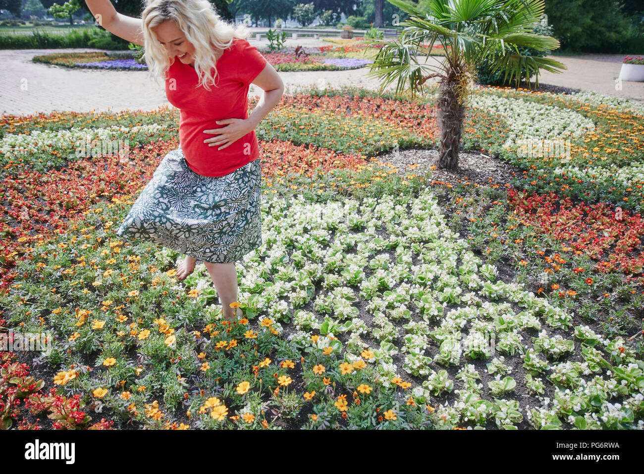 Felice donna incinta a piedi attraverso fiori che sbocciano in posizione di parcheggio Foto Stock