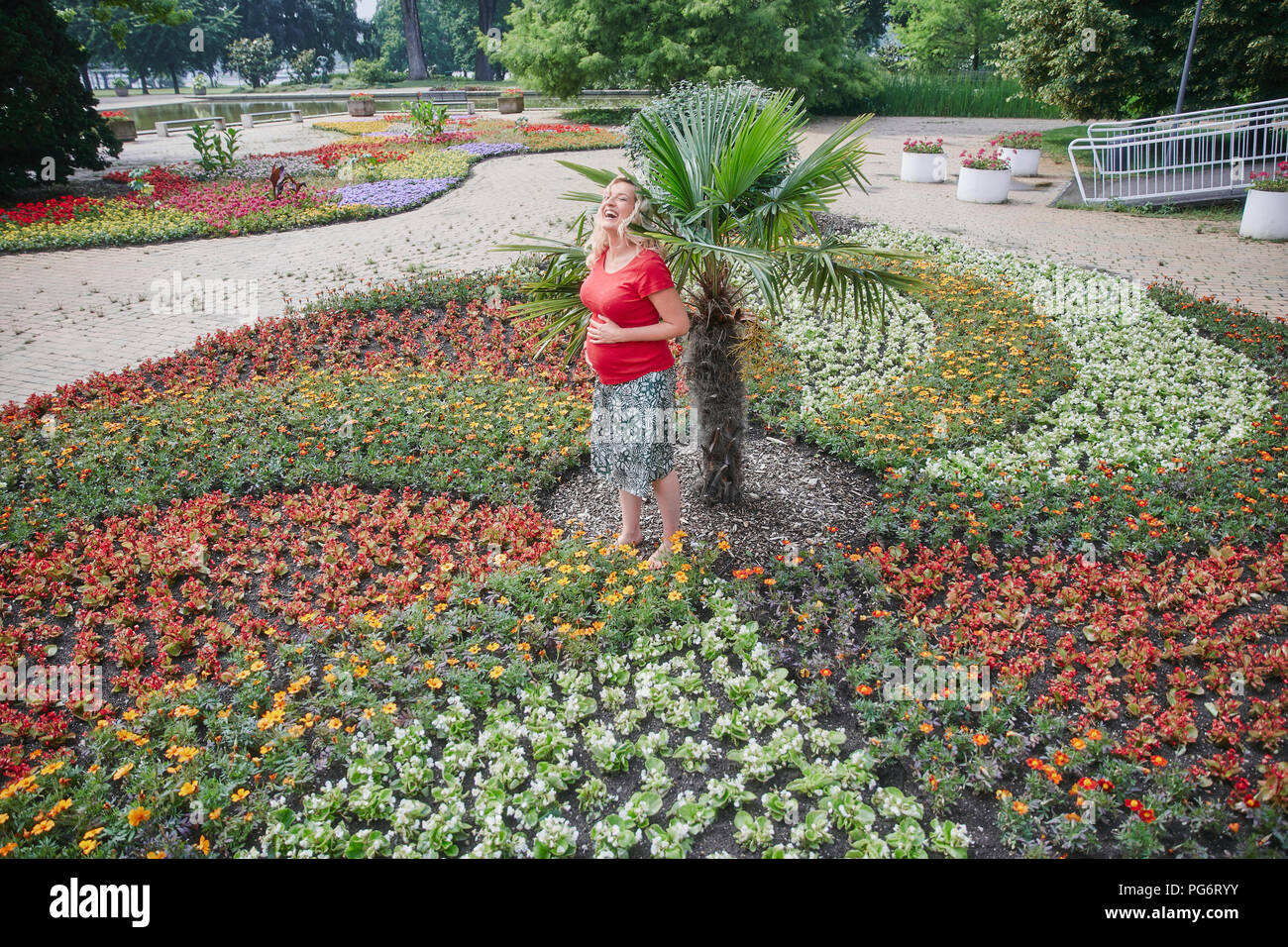 Felice donna incinta in piedi in mezzo a fiori che sbocciano in posizione di parcheggio Foto Stock