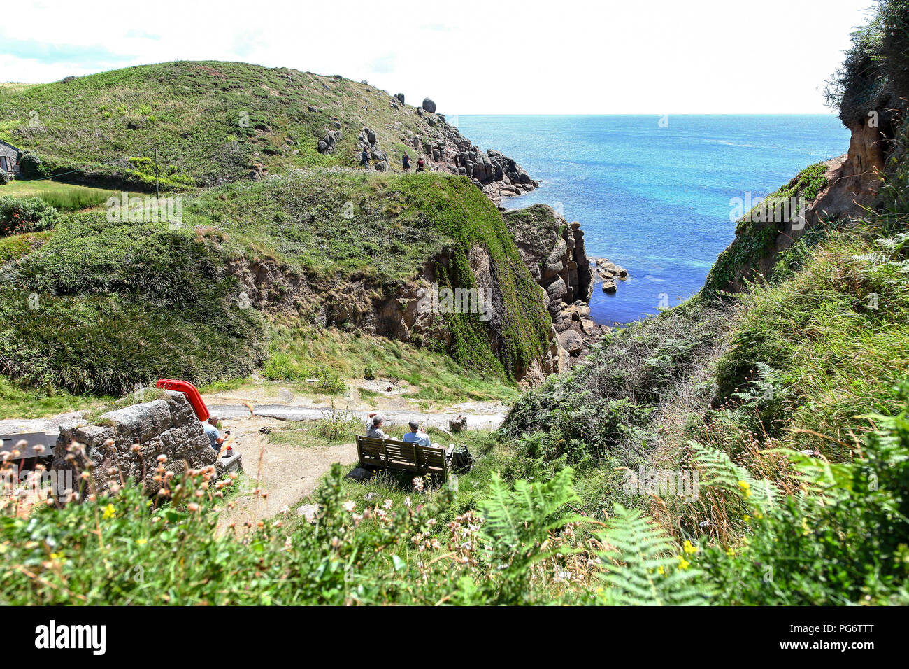La gente seduta un banco che guarda al mare a Porthgwarra Cove, Porthgwarra, Cornwall, South West England, Regno Unito Foto Stock
