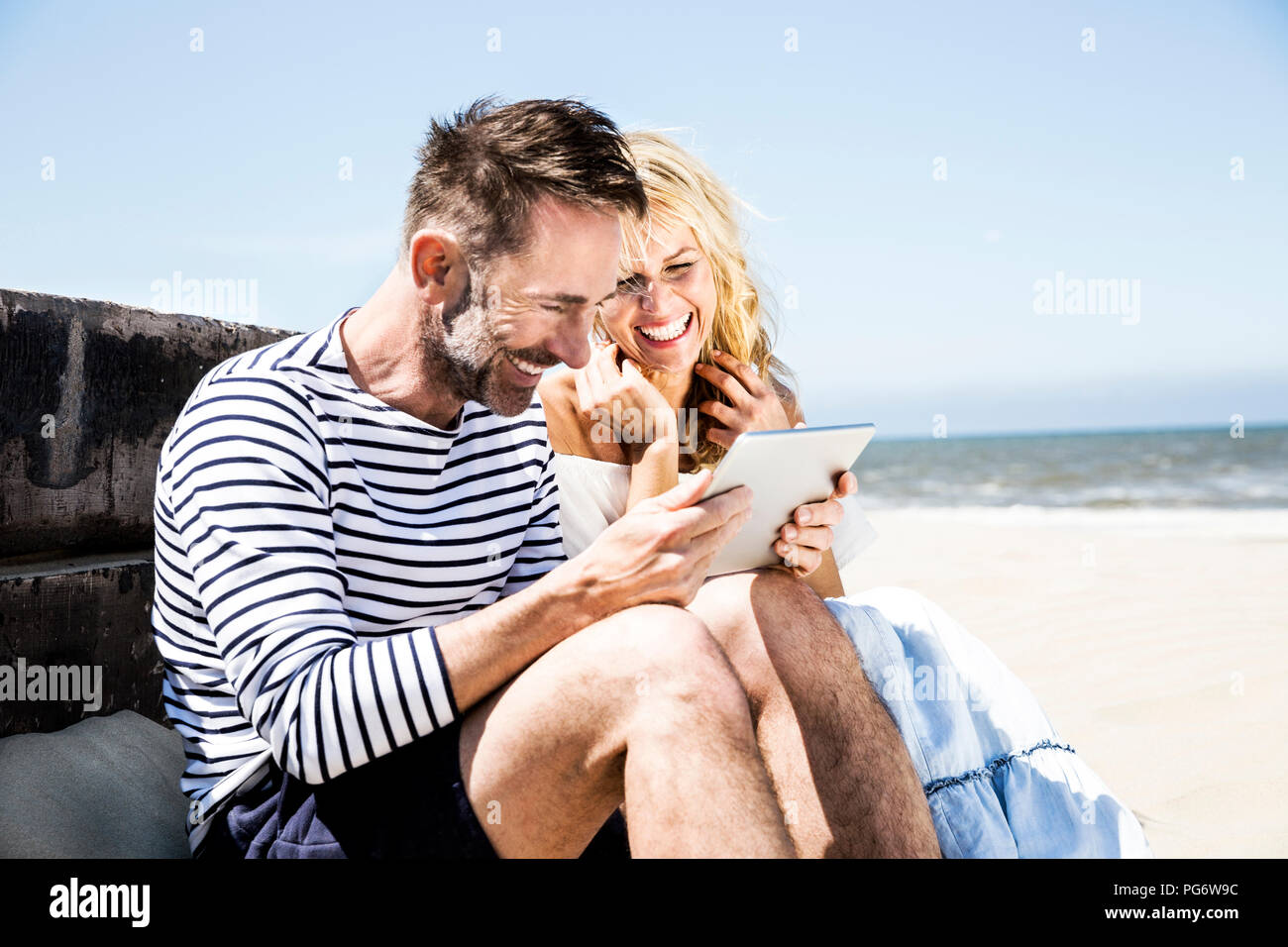 Coppia felice sulla spiaggia guardando tablet Foto Stock