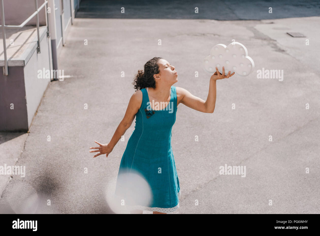 Donna in piedi nel cortile, azienda simbolo di cloud, soffiando kiss Foto Stock