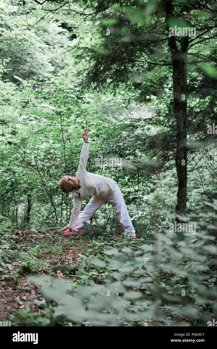 Senior donna fare yoga nella foresta, triangolo pongono Foto Stock
