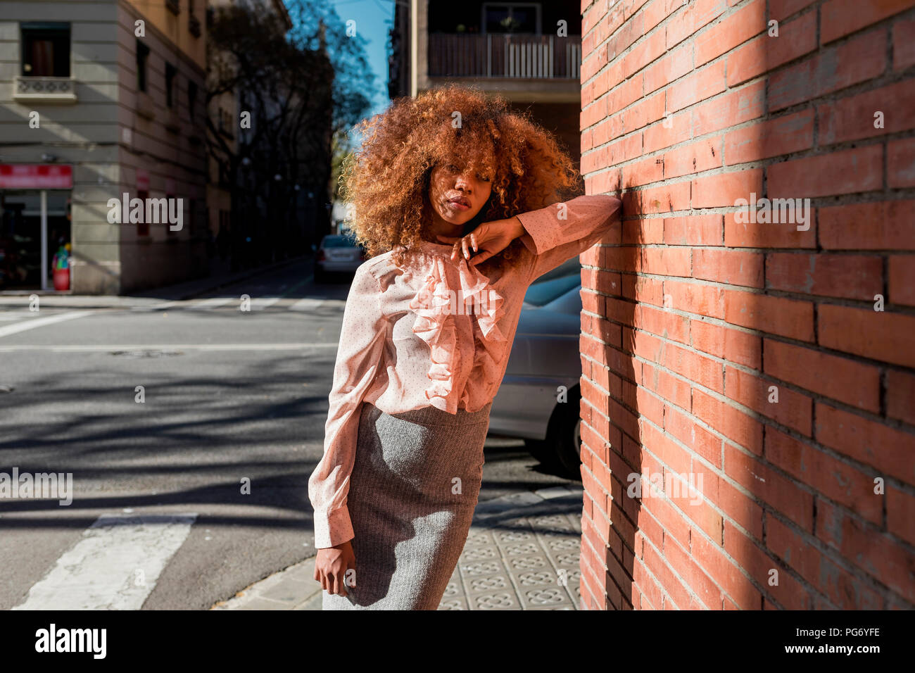 Ritratto di giovane e bella donna con taglio di capelli afro appoggiata contro un muro di mattoni in città Foto Stock