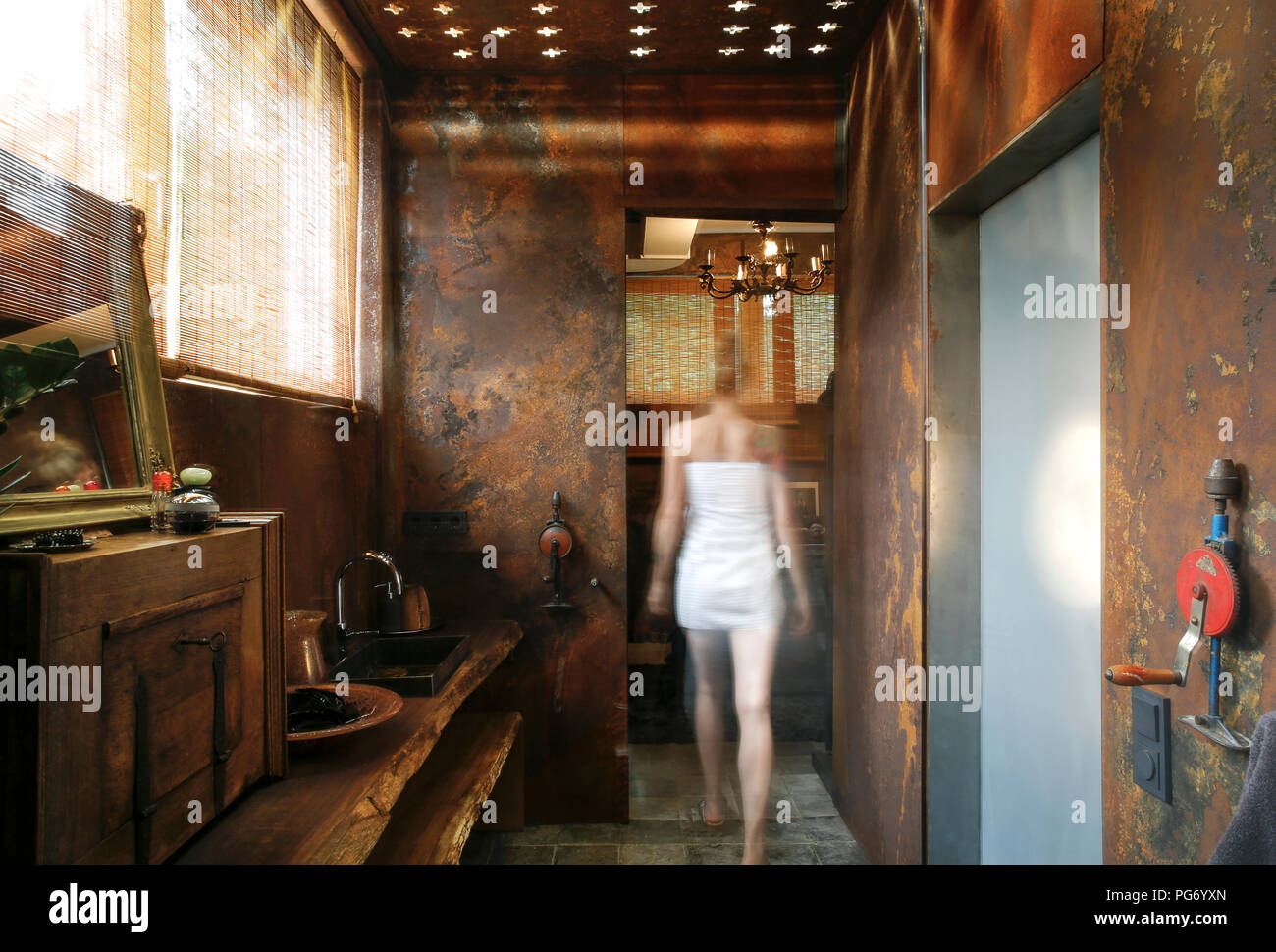 Vista posteriore della donna che cammina in bagno con in acciaio corten rivestimento pareti e soffitto effetti di luce Foto Stock