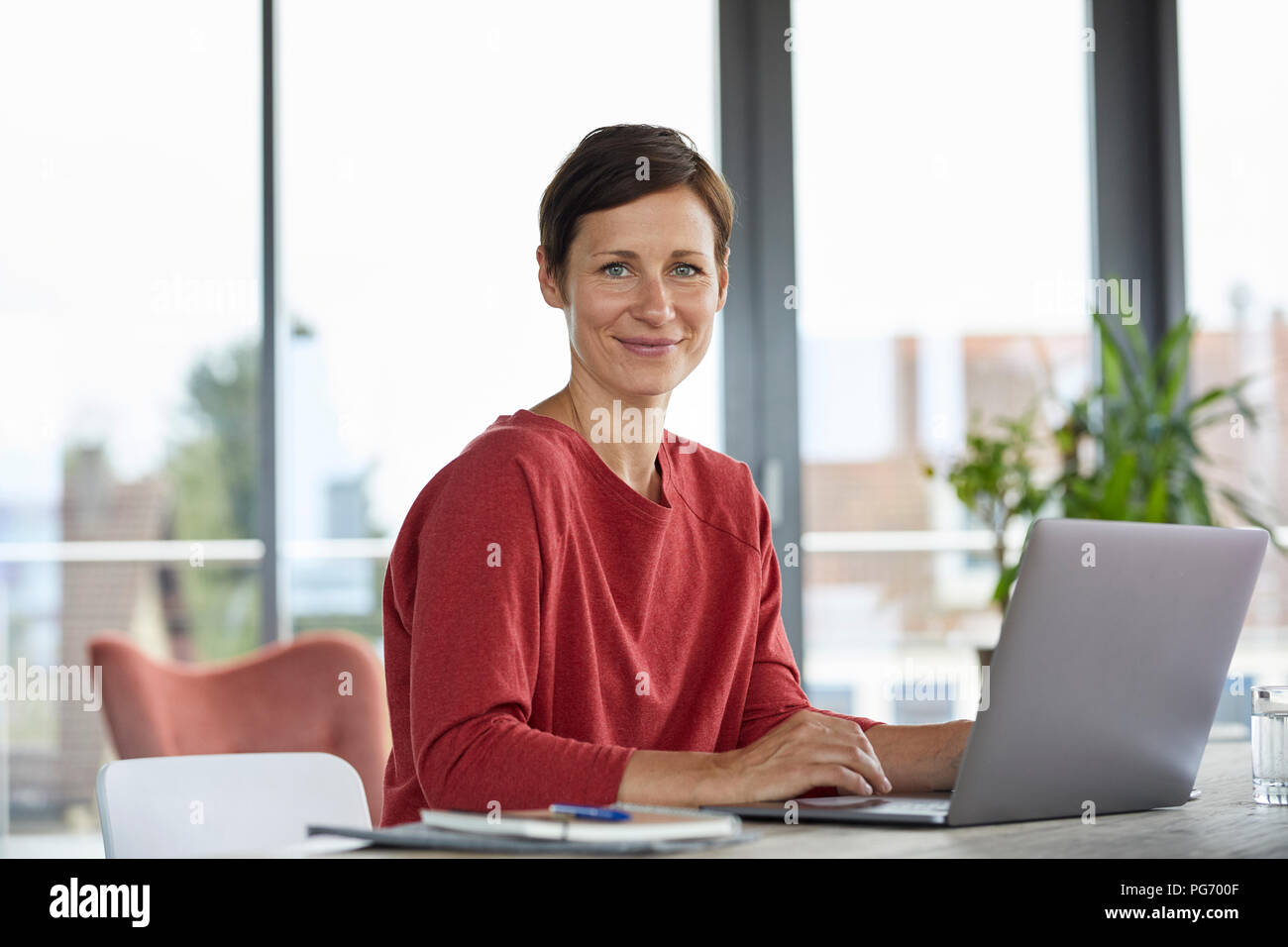 Ritratto di donna sorridente seduta a tavola a casa utilizzando laptop Foto Stock