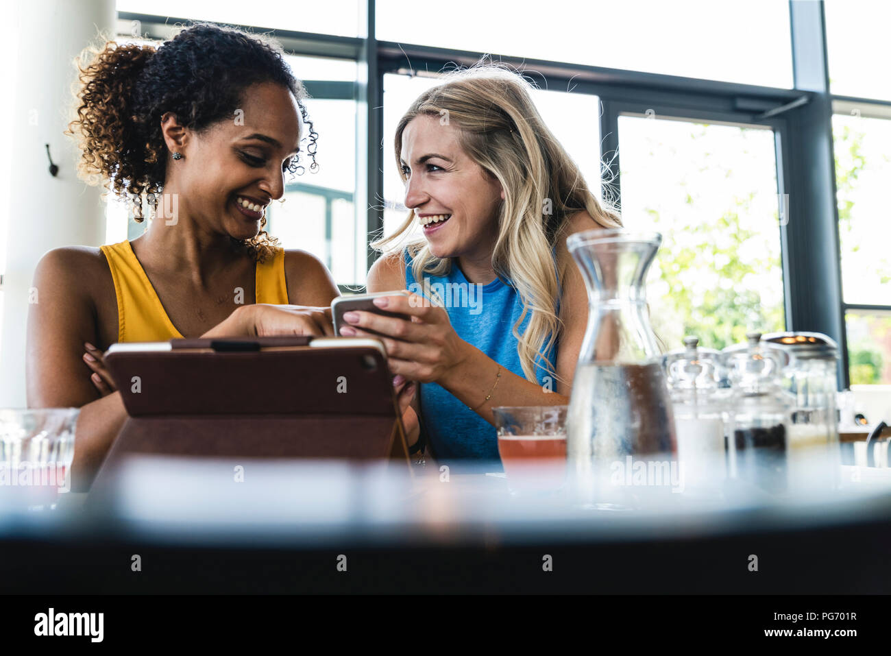 Migliori amici riuniti in cafe, parlare e condividere notizie, utilizzando tavoletta digitale Foto Stock
