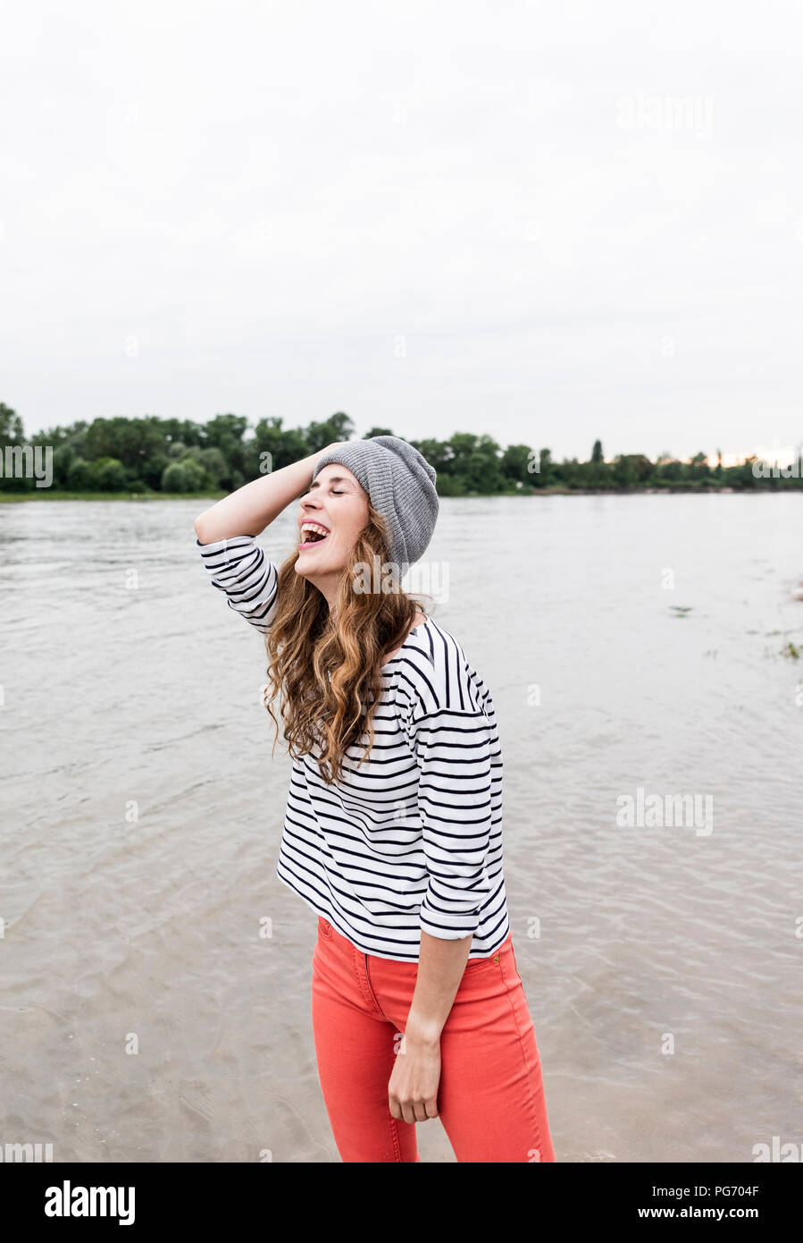 Ridendo donna che indossa wooly hat in corrispondenza di un fiume Foto Stock