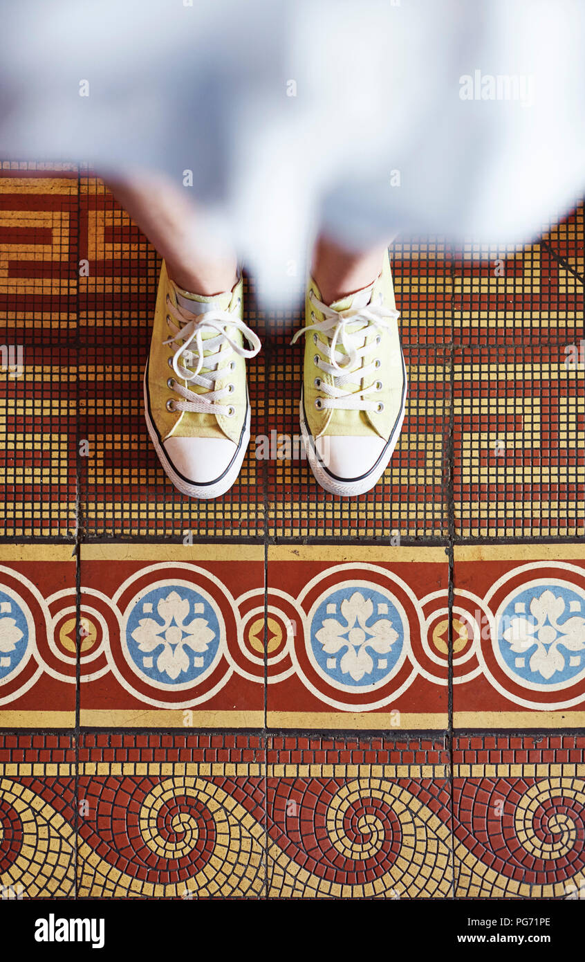 Donna che indossa sneakers giallo in piedi sul pavimento a mosaico, vista parziale Foto Stock