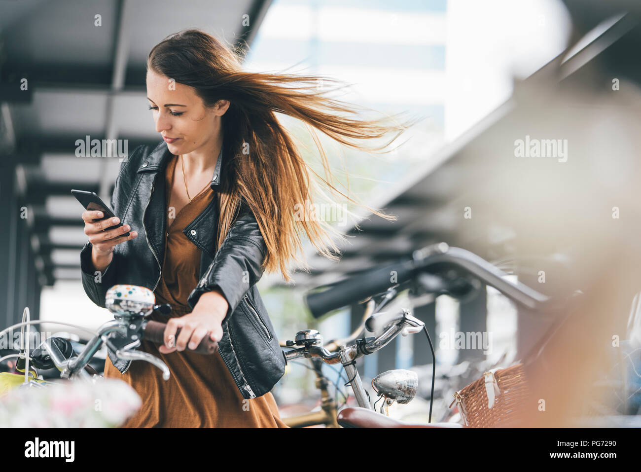 Giovane donna con la bicicletta utilizzando il cellulare in città Foto Stock