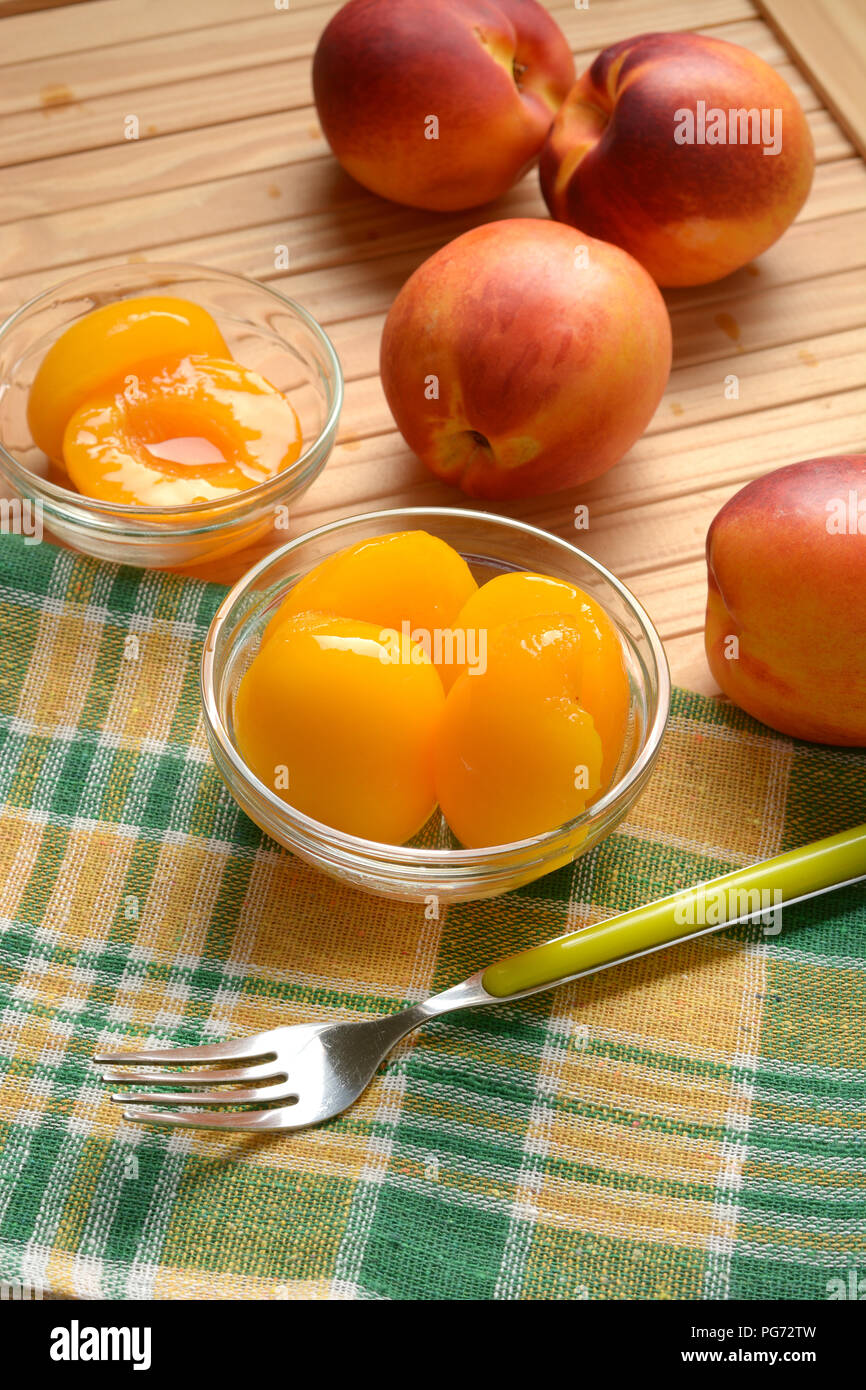 Le pesche allo sciroppo nella vaschetta di vetro con frutta intorno - primo piano Foto Stock