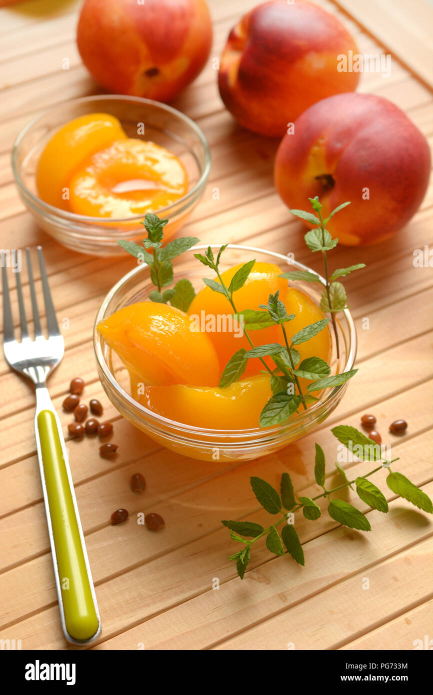 Le pesche allo sciroppo nella vaschetta di vetro con frutta intorno - primo piano Foto Stock