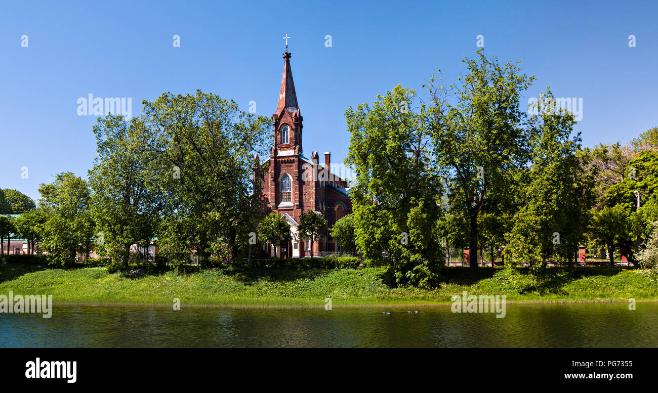 Sulla riva del lago tra il verde lussureggiante di alberi in estate nelle giornate di sole vi è un mattone di Cattolica da un rosso mattone in Pushkin, San Pietroburgo, Foto Stock