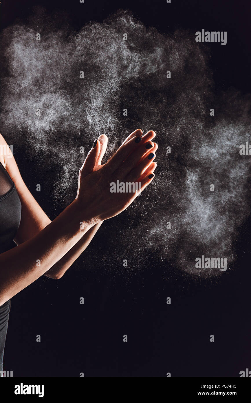 Immagine ritagliata di sportive diffusione di polvere di gesso in mani, sfondo nero Foto Stock