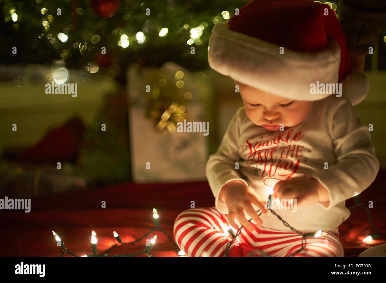 Bambina gioca con le luci di Natale con un cappello da Babbo Natale. Foto Stock