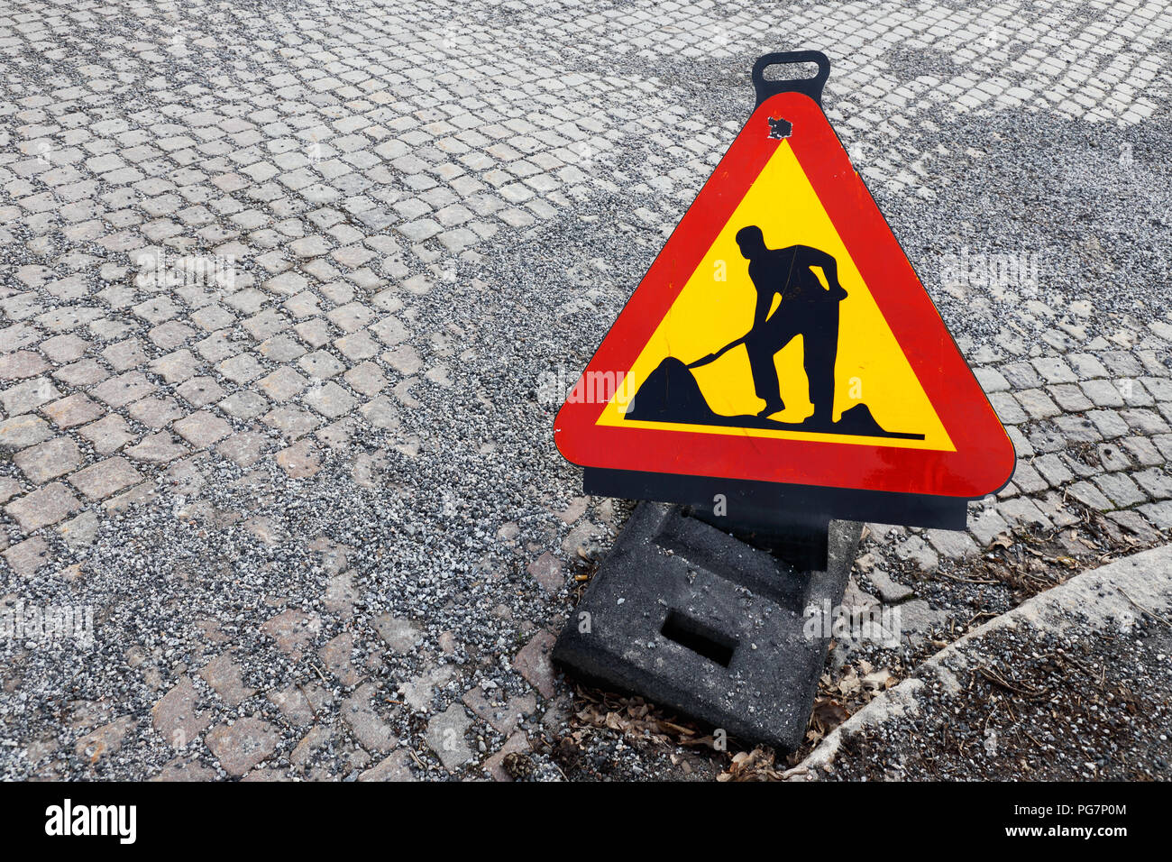 Angelo alta vista di un triangolo a forma di lavori temporanei cartello segnaletico posto su una strada pavimentata con cobbelstones con ghiaia sulla parte superiore. Foto Stock