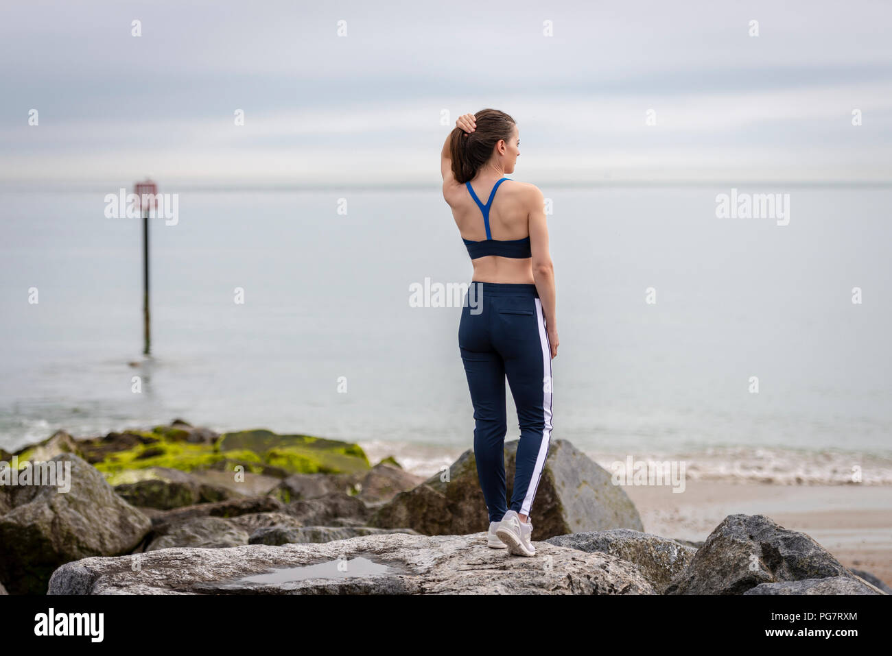 Sportivo da donna che indossa abbigliamento sportivo in piedi sulle rocce dal mare regolando i suoi capelli prima di esercizio. Foto Stock