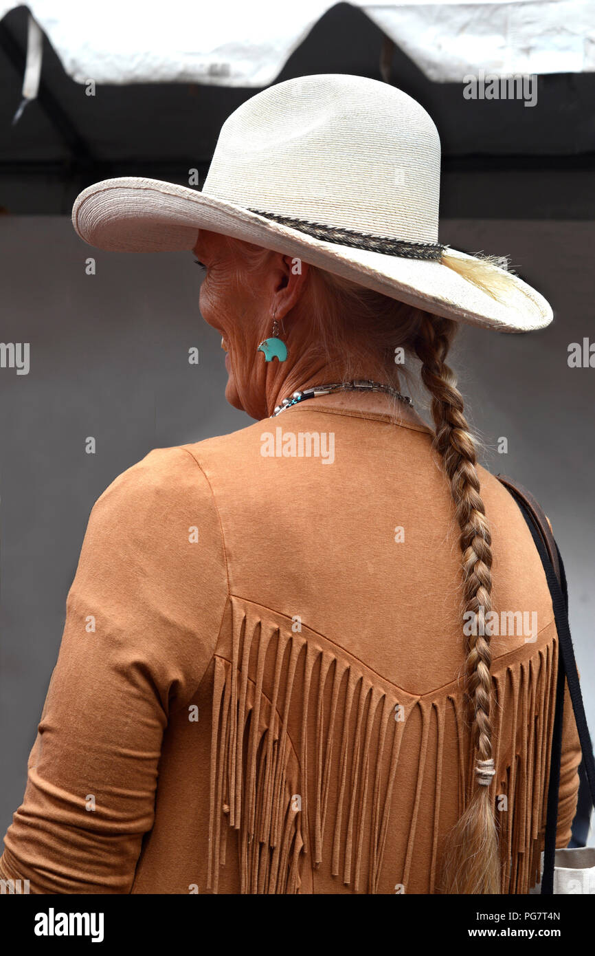 Una donna con capelli intrecciati e indossando western abbigliamento e gioielli visita un outdoor art show a Santa Fe, New Mexico. Foto Stock