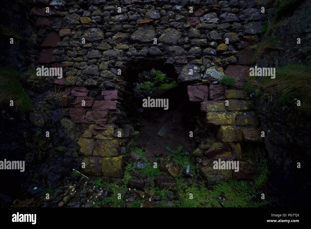 Misterioso buco in un muro, che conduce alla vegetazione verde. Un buco in un edificio fortificato abbandonato fatto di roccia. Rovine storiche del forte di roccia derelict. Foto Stock