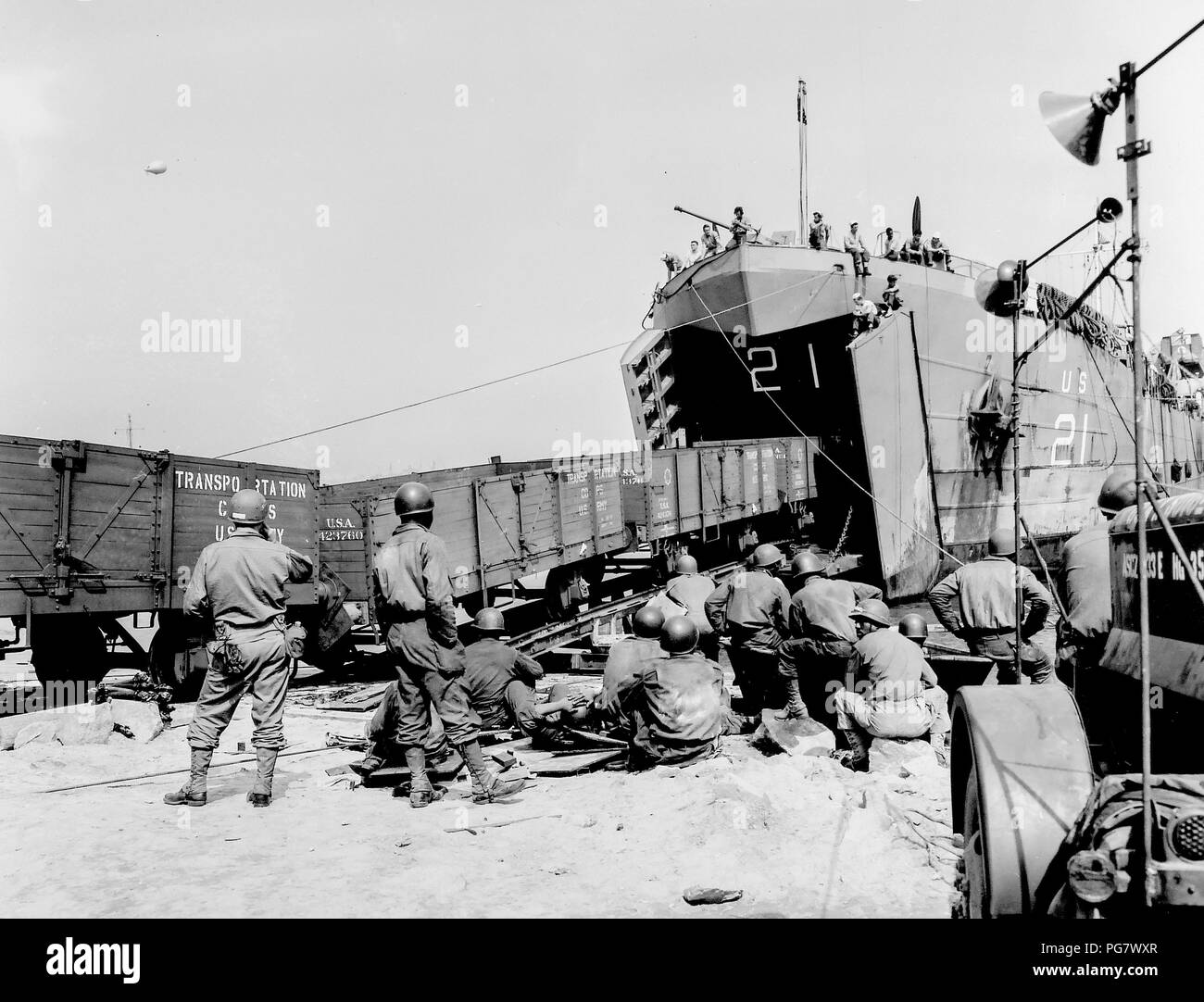 [Didascalia originale: ]I GUARDACOSTE LINKS britannica e francese ferrovie: fuori del massiccio di ganasce di un U.S. Coast Guard-presidiati (LST) (sbarco navi, cisterne) rotoli di una stringa di vagoni ferroviari, caricato con vitale bellica in Inghilterra e consegnati in Francia. Il Coast Guard-presidiati nave Traghetti materiale rotabile da un porto britannico di una spiaggia francese del fungo, formando un collegamento mobile tra le ferrovie dei due paesi. Ore di inestimabile valore, lo scarico e il ricarico, vengono salvati eseguendo il pranzo di auto in pista attrezzata tank deck del LST e il trasporto attraverso il canale della Manica a rotolare giù per un Foto Stock